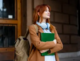 a young woman with red-hair holds a binder outside